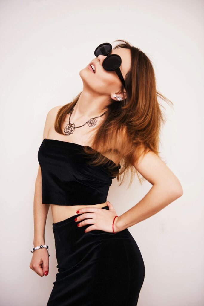 Elegant woman posing in black outfit and sunglasses, exuding modern style.